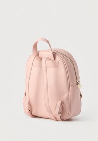 Mochila de cuero sintético rosa con forma redondeada, dos asas superiores y una cremallera dorada. Cuenta con un pequeño colgante en forma de corazón en el tirador de la cremallera.
