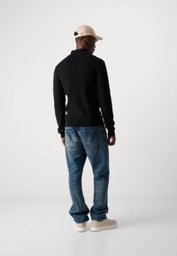 Black knit sweater, light denim jeans, and beige sneakers. The sweater features a high collar; the jeans have a classic five-pocket design.