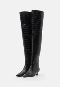 Bottes noires arrivant au genou en simili-cuir crocodile texturé, avec des bouts pointus et de petits talons carrés, présentant un détail de fermeture éclair sur le côté.