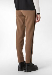 Bruine broek met een slim fit, voorzien van een zwarte zijstreep, gemaakt van zachte stof. Gecombineerd met zwarte, instap enkellaarsjes.