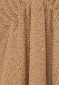 Tissu tricoté brun clair avec motifs en losanges et rayures, montrant une texture douce et des plis drapés.