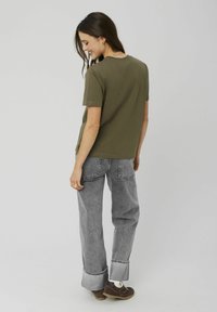 T-shirt en coton vert olive avec une coupe décontractée, assortie à un jean en denim gris taille haute avec un ourlet replié et des détails de couture subtils.