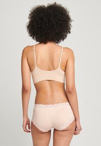 Conjunto de sujetador beige y braguitas con bordes de encaje, que presenta una tela suave, tirantes ajustables y un delicado acento de encaje floral en la cinturilla.