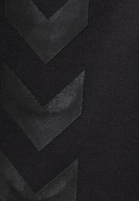 Svart textil med upphöjda, matta svarta chevronmönster. Ytan är slät med en något texturerad, kontrasterande bakgrund.