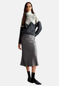 Maglione a collo alto grigio e bianco a fantasia con polsini a costine, abbinato a una raffinata gonna midi in satin grigia e mocassini neri texturizzati.