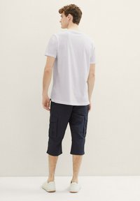 Weißes Kurzarm-T-Shirt, kombiniert mit marineblauen Cargo-Shorts. Die Cargo-Shorts verfügen über mehrere Taschen; das Model trägt weiße Sneakers. Einfaches, lässiges Design.