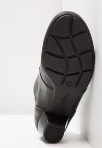 Černá kožená podrážka boty s gumovým vzorkem, s obdélníkovým podpatkem, hladkým povrchem a otiskem značky. Vyrobeno v Portugalsku.