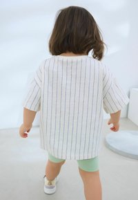 Kortærmet, stribet skjorte i lys cremefarve med blå lodrette streger, parret med mintgrønne shorts og hvide sneakers.