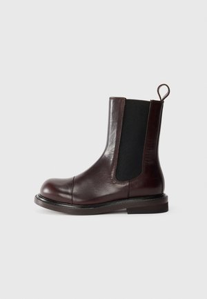 Braune Leder Chelsea-Stiefel mit elastischen Seiteneinsätzen, abgerundeter Spitze und einer Schlaufe auf der Rückseite. Flache Gummisohle. Glatte Textur.