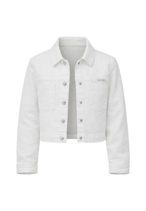 Giovane ragazza con capelli castani, giacca di jeans bianca, camicia bianca, jeans larghi azzurri chiari e sandali neri, in piedi con una mano in tasca.