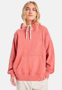 Pink hoodie made of soft, textured fabric. Features a drawstring hood, kangaroo pocket, and ribbed cuffs. Subtle logo on chest.