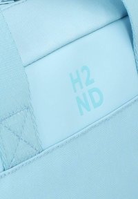Borsa di tessuto azzurro chiaro con una base rettangolare liscia e rigida, con il testo "H2ND" impresso in un blu leggermente più scuro.