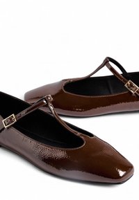 Bailarinas de charol marrón con diseño de tira en T y punta cuadrada. Presentan una hebilla de tono dorado en la tira. Textura suave y brillante.