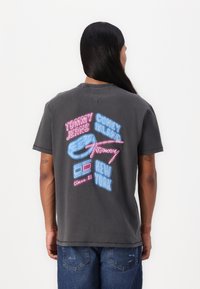 Grå bomulds t-shirt med multikolor grafisk tekst og ikoner bagpå, herunder "CONEY ISLAND," "TOMMY JEANS," og en donut-illustration.