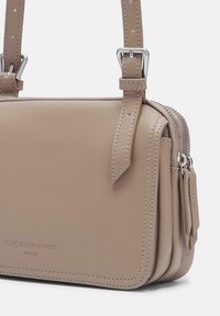 Borsa a tracolla in pelle beige con chiusura a zip, tracolla regolabile e accessori in metallo argentato. Presenta un design a strati e dettagli di cucitura discreti.