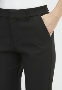 I pantaloni neri su misura presentano una texture liscia, tasche anteriori e un design aderente. La vita è piatta, offrendo una silhouette elegante.