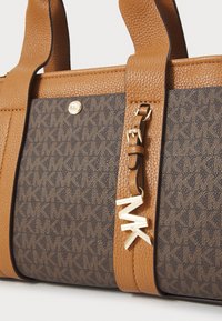 Borsa in pelle marrone con un pannello testurizzato marrone scuro con un motivo a logo, hardware dorato e un'etichetta d'accento con la scritta "MK."