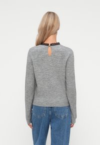 Grijze trui met lange mouwen, een sleufdetail aan de achterkant en zwarte kant rondom de halslijn. Draag het met hoge taille blauwe jeans.