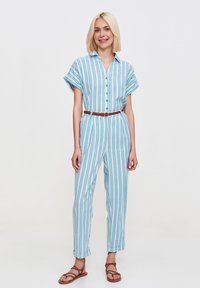 Pasiasty kombinezon w jasnoniebieskim i białym kolorze, krótkie rękawy, zapięcie na guziki z przodu, ściągnięta talia brązowym paskiem, luźny krój, długość do kostek, casualowy styl.