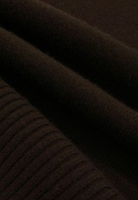 Tejido de color marrón trenzado que presenta una textura suave y acanalada. El material parece suave y está dispuesto en pliegues.