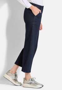 Jean en denim foncé avec une coupe droite et des poches latérales, associés à des baskets argentées et beiges avec des accents métalliques et un tissu texturé.