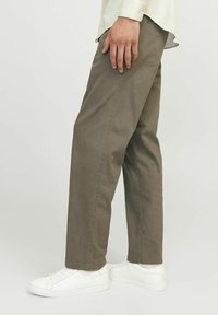 Olivgrüne Baumwollhosen mit lockerer Passform. Verfügt über seitliche Taschen und subtile Nähdetails. Kombiniert mit weißen Sneakers.