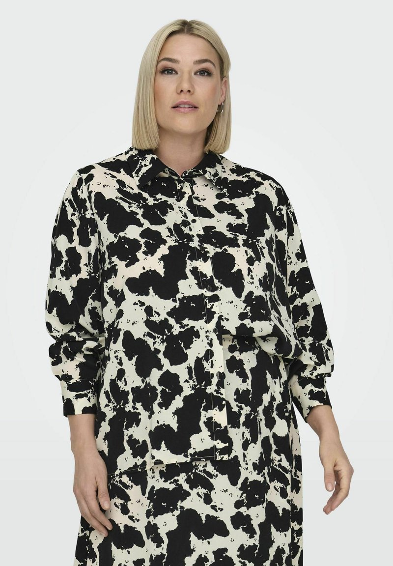 Sort og hvid prikket skjorte lavet af et letvægtsstof. Den har en krave, knaplukning foran og lange ærmer med løst fit.