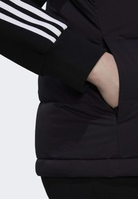 Zwarte gewatteerde jas met een ritszak, voorzien van een stevige textuur en witte strepenaccenten op de mouw. Slim fit ontwerp.