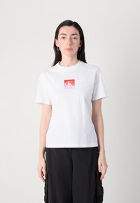 Witte katoenen t-shirt met korte mouwen en een ronde halslijn, met een rood-witte gradient "cK" logo op de voorkant.