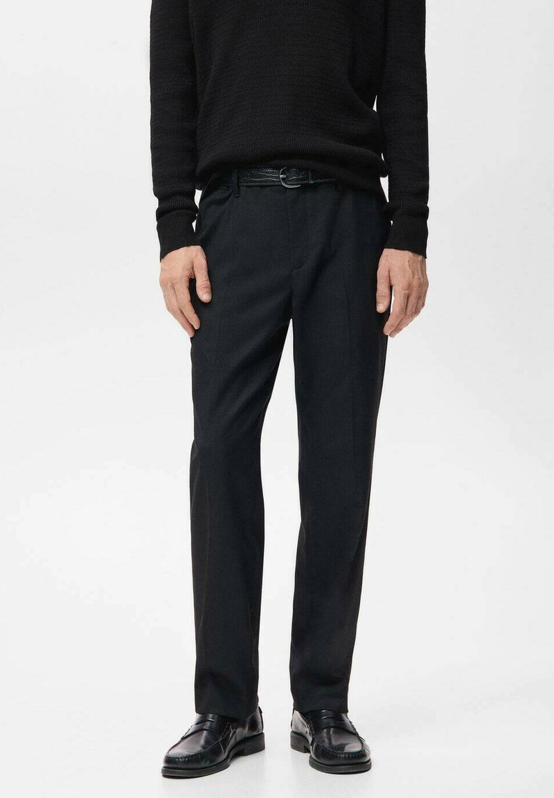 Černé kalhoty z hladkého materiálu s klasickým střihem a předním záhybem, doplněné černým páskem a leštěnými černými botami.