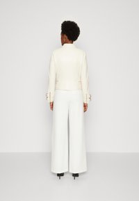 Veste en cuir blanc au design ajusté, avec des accents en métal doré. Associée à un pantalon blanc à jambes larges et des escarpins noirs.