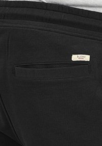 Pantalons noirs en tissu texturé, dotés d'une poche arrière et d'une étiquette sur laquelle est inscrit "BLEND" en crème avec des accents rouges.