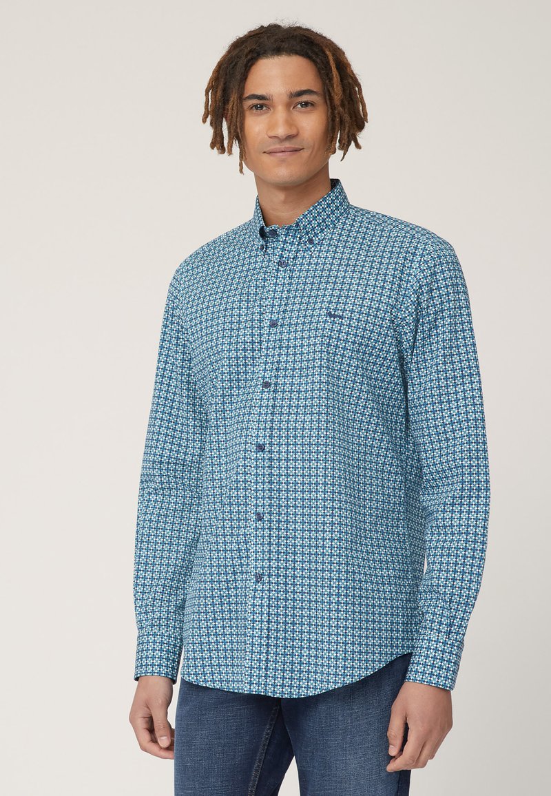 Camicia a pattern blu e bianco con colletto button-down, maniche lunghe e orlo curvo. Presenta una tasca sul petto. Il tessuto appare liscio.