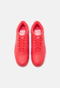 Ζευγάρι κόκκινων δερμάτινων αθλητικών παπουτσιών Reebok με κορδόνια, διάτρητες μύτες και λογότυπο στη γλώσσα και τις πλαϊνές επιφάνειες, εμφανιζόμενα από πάνω σε λευκό φόντο.