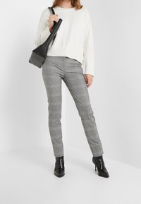 Krämfärgad stickad tröja med ribbad nederkant, grå rutiga skräddarsydda byxor och svart läderhandväska med lång form, i kombination med svarta ankelstövlar med klack.