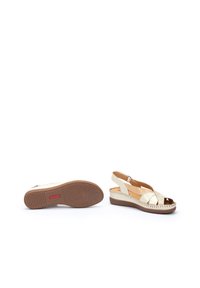 Sandalias de cuña blancas con punta abierta, que cuentan con tiras entrelazadas y suelas de goma marrón. Costura decorativa a lo largo del borde de la suela.