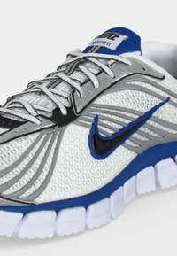 Λευκό, γκρι και μπλε sneaker Nike Skylon 11 με επάνω μέρος mesh, μαύρο λογότυπο swoosh, λευκά κορδόνια και χωριστή λευκή σόλα με μπλε λεπτομέρειες στη μεσαία σόλα.