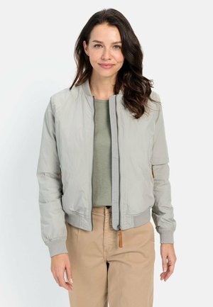 Lichtgrijze bomberjack met een ritssluiting aan de voorkant, ribbelmanchetten en een ribbelzoom. Gecombineerd met een groene top en beige broek, met een gladde, glanzende textuur.