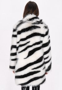 Sort og hvid faux fur frakke med et stribet mønster, lange ærmer og en bred krave, der har en blød, tekstureret finish.