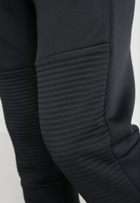 Svarta träningsbyxor har ett slätt tyg med ribbade paneler vid knäna. Designen betonar en smidig, figurnära silhuett.