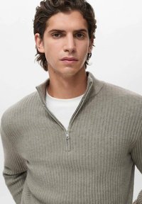 Pullover grigio chiaro a costine con collo con zip, realizzato in tessuto testurizzato. Indossato sopra una maglietta bianca a girocollo, vestibilità slim.