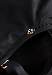 Gros plan sur un tissu noir avec un détail de couture et une petite boucle circulaire dorée attachée à une sangle.