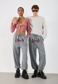 Rød rutete croppet topp med knytning foran, kombinert med grå joggebukser med svart grafisk tekst. Modellene har på seg svarte støvler og solbriller.