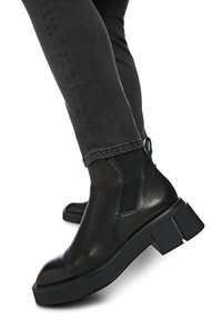 Schwarze Leder-Stiefeletten mit einer klobigen, strukturierten Sohle, elastischen Seitenteilen, abgerundetem Zehenbereich und kontrastierenden Gummi-Absatz-Akzenten.