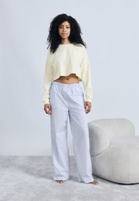 Ανοιχτό κίτρινο cropped φούτερ με τσέπη στο στήθος, συνδυασμένο με άνετο παντελόνι πιτζάμας με μπλε και λευκές ρίγες. Μαλακή υφή, καθημερινή εφαρμογή.