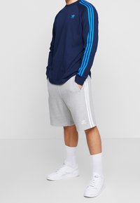 Camisa de manga larga azul marino con rayas, pantalones cortos grises con rayas blancas y zapatillas blancas; look de deporte casual.