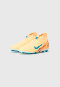 Žluté fotbalové kopačky se štíhlým designem, vybavené modrým logem Nike a tyrkysovými akcenty. Texturovaný svršek s těsným fit.
