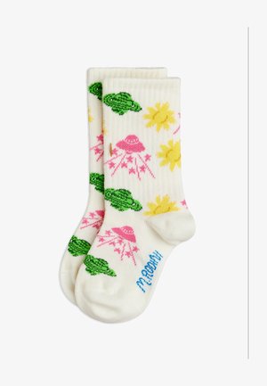 Άσπρες κάλτσες με πολύχρωμα σχέδια πράσινων χελωνών, κίτρινων ήλιων και ροζ ιπτάμενων δίσκων που εκπέμπουν ακτίνες, με μπλε κείμενο κοντά στα δάχτυλα.