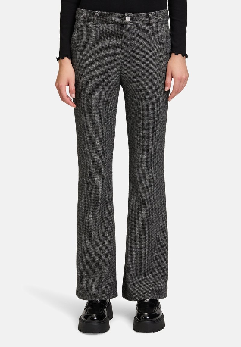Femme portant un pantalon droit gris texturé avec une fermeture à boutons et des chaussures à plateforme noires épaisses sur fond blanc.