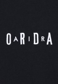 Svart tyg med vit broderad text som säger "OARIDRA," med varierande bokstavsstorlekar och en lätt texturerad finish.